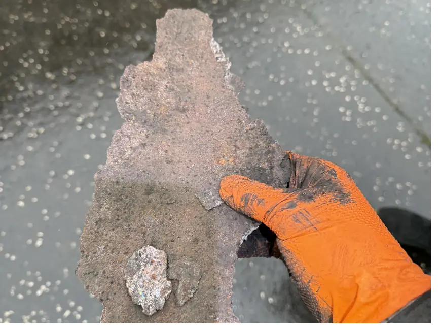 Section of flue wall lost to corrosion, held in a gloved hand